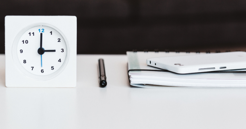 Clock on desk with pen and paper